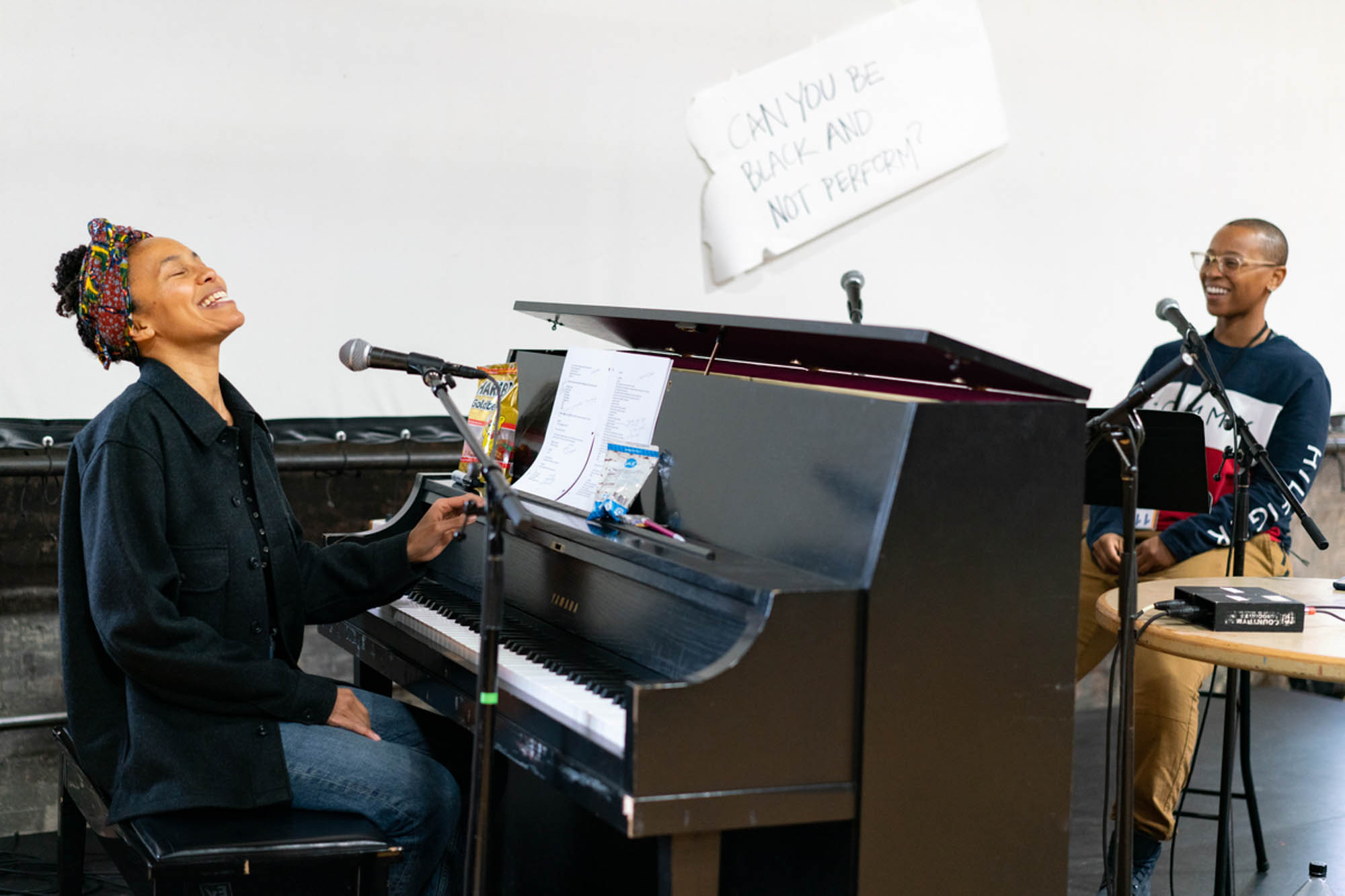 two black women laugh at their microphones as they create music together