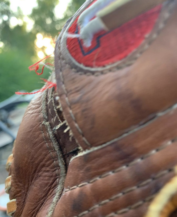 Tight, abstracted shot of a classic brown baseball glove. The red logo is frayed. Sun peaks through in the tiny background.