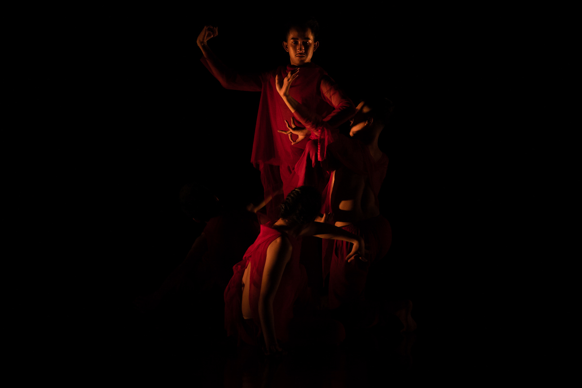 Prumsodun Ok & NATYARASA dancers, wearing diaphanous costumes of red cloth, perform Drops & Seeds on a dark stage at the Department of Performing Arts, Cambodia.