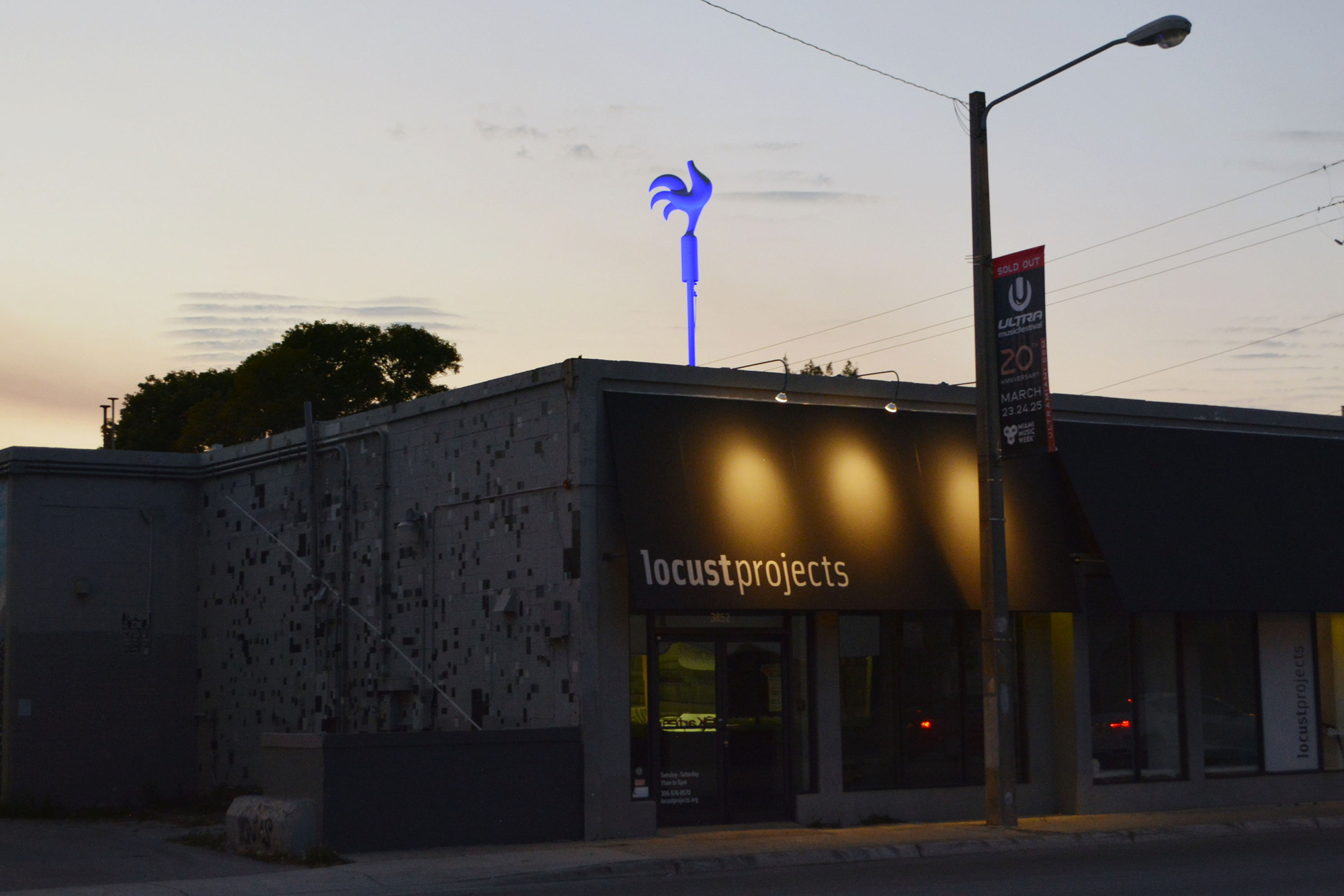 A photograph of a single-story, storefront building with a streetlight out front. An awning on the building has text that reads,