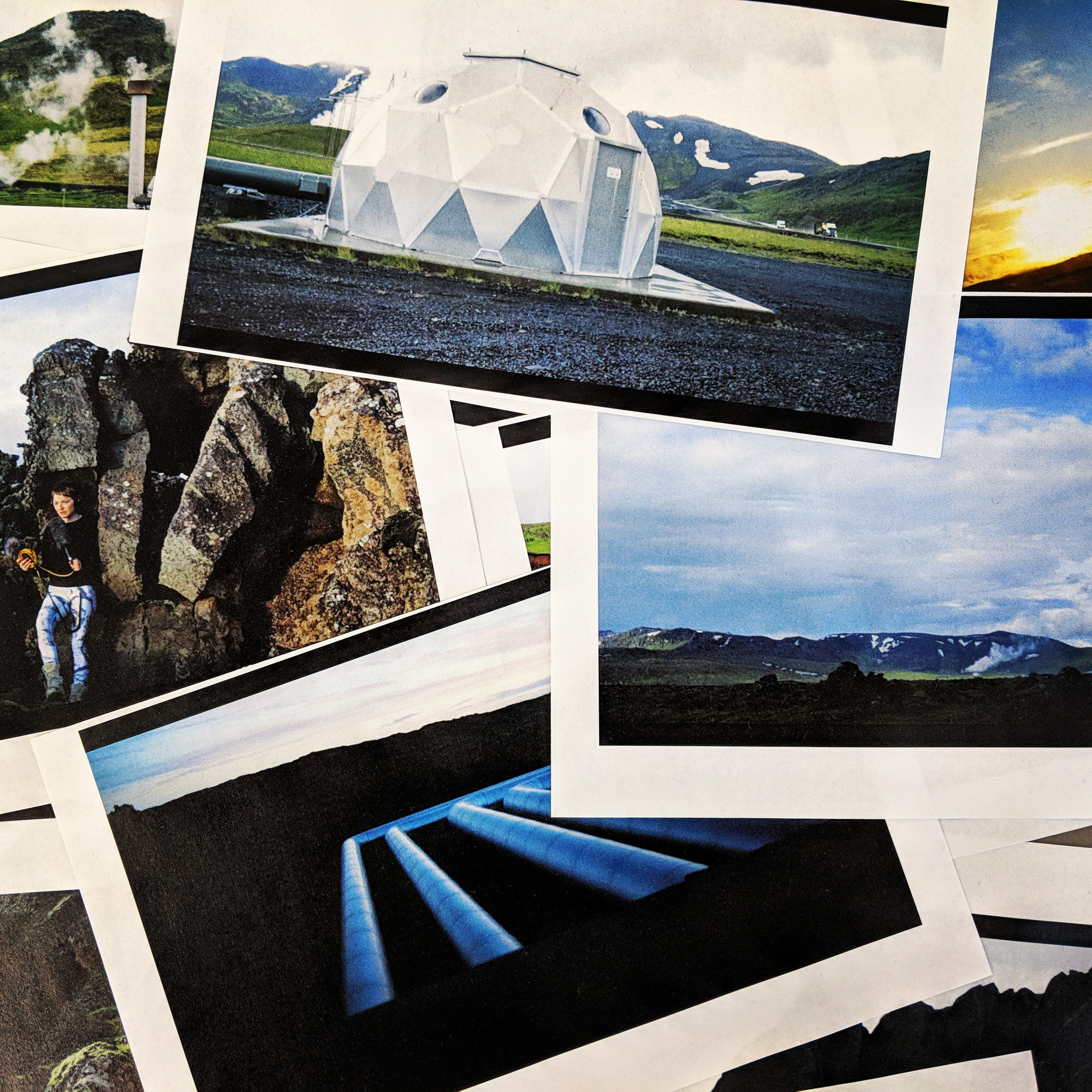Several video stills printed on paper are scattered haphazardly in a pile. Among them: a silver geodesic dome, a person nestled into a rock speaking into a microphone, large pipes and steaming geysers.