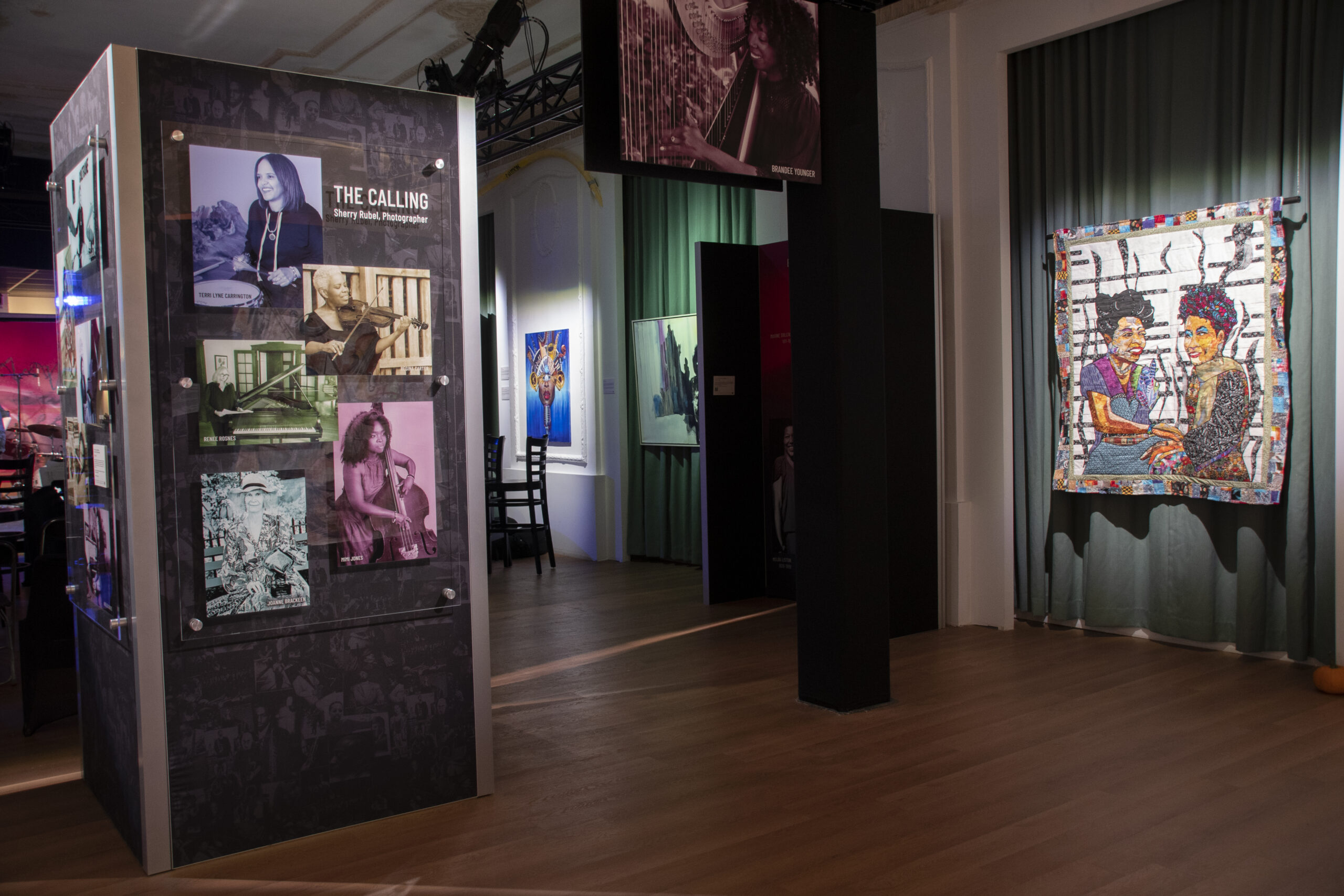 View of exhibit, including pieces from photo collection “30 Influential Woman Instrumentalists” by Sherry Rubel, and quilt “Mary Lou Meets Geri Allen” by Ramsess
