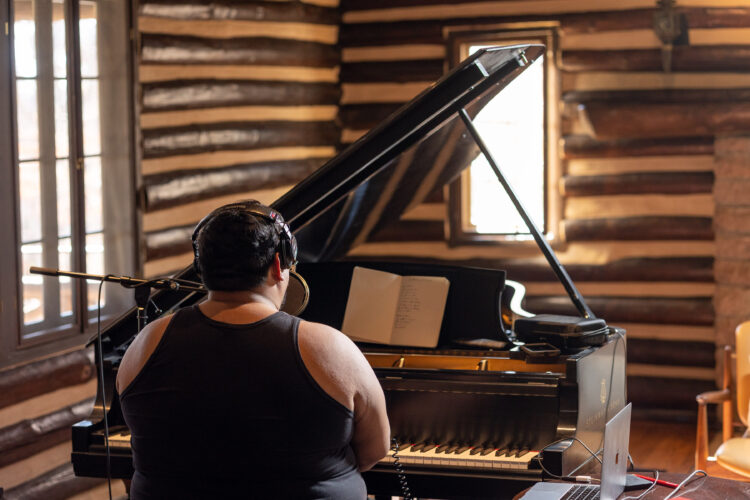 Dorian Wood sits at a piano in a wood-paneled room.