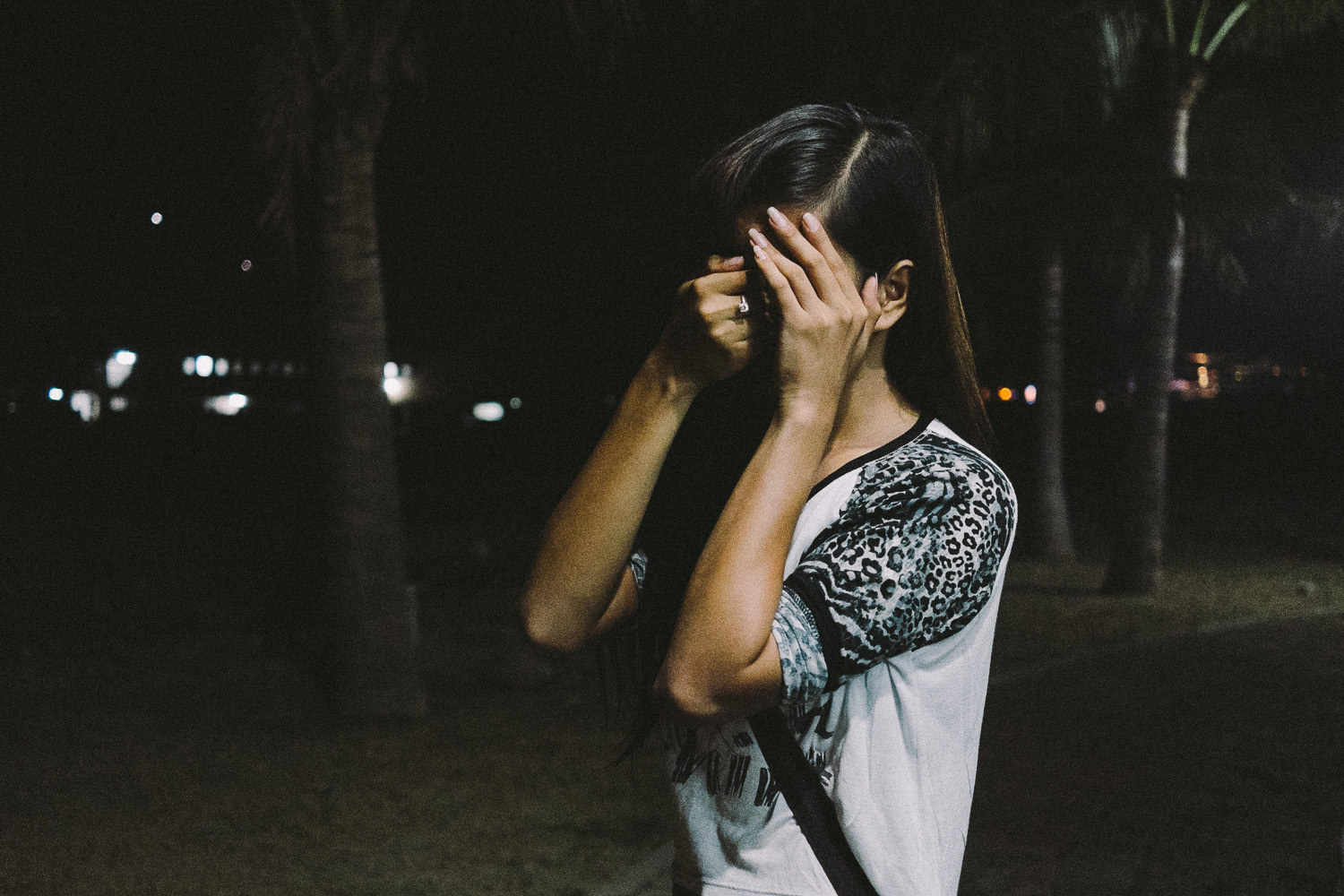 A young trans woman in Olongapo City, Philippines at night, covering her face with her hands while posing for a picture.