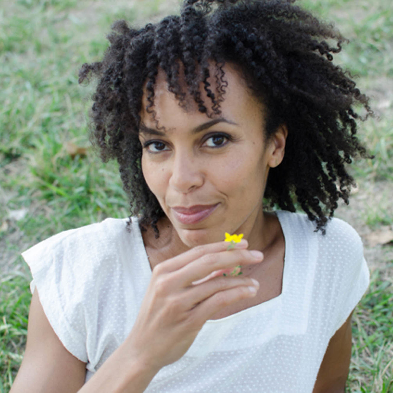 A black woman with curls tumbling in the wind has just smelled a delicate yellow flower and reveals an inner pleasure from the scent
