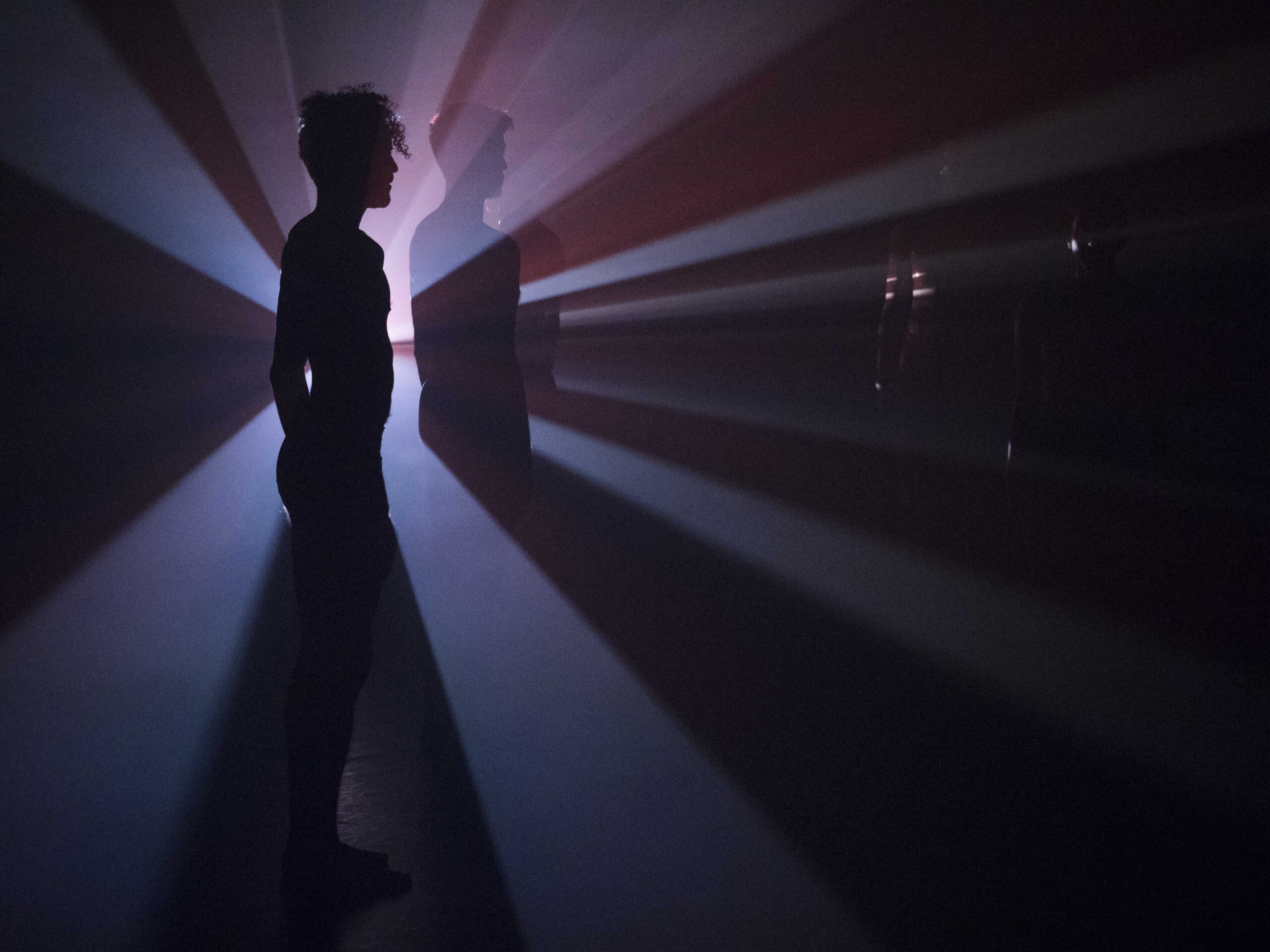 Five performers stand still with video projection in which reddish halos shine from their behind.