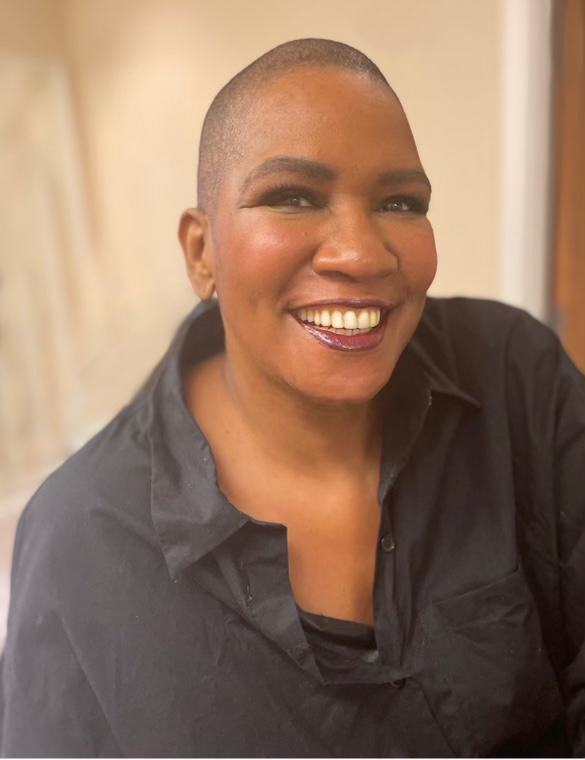 Image of a dark brown skinned Black woman with a shaved head big smile black shirt.