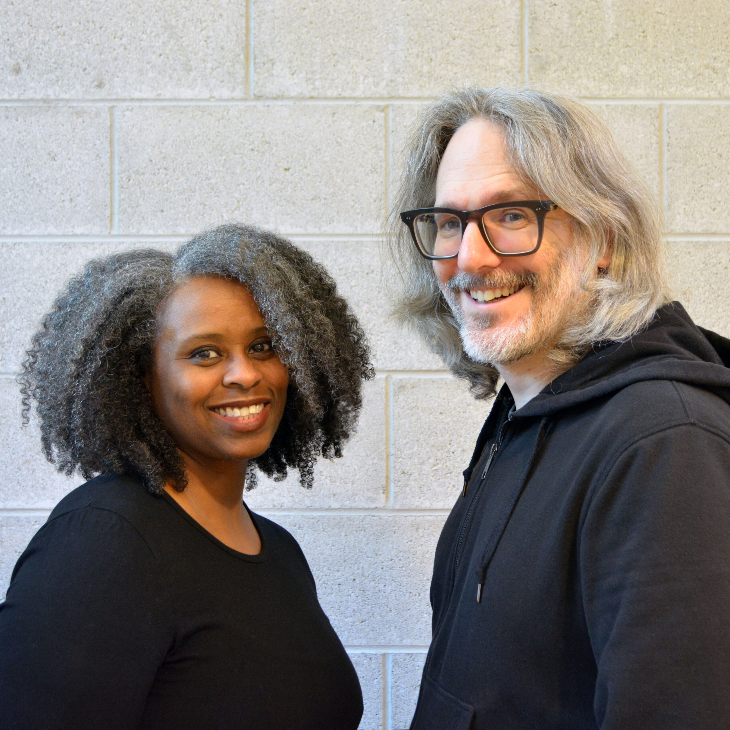 A Black woman and a white man look directly at the viewer and smile.