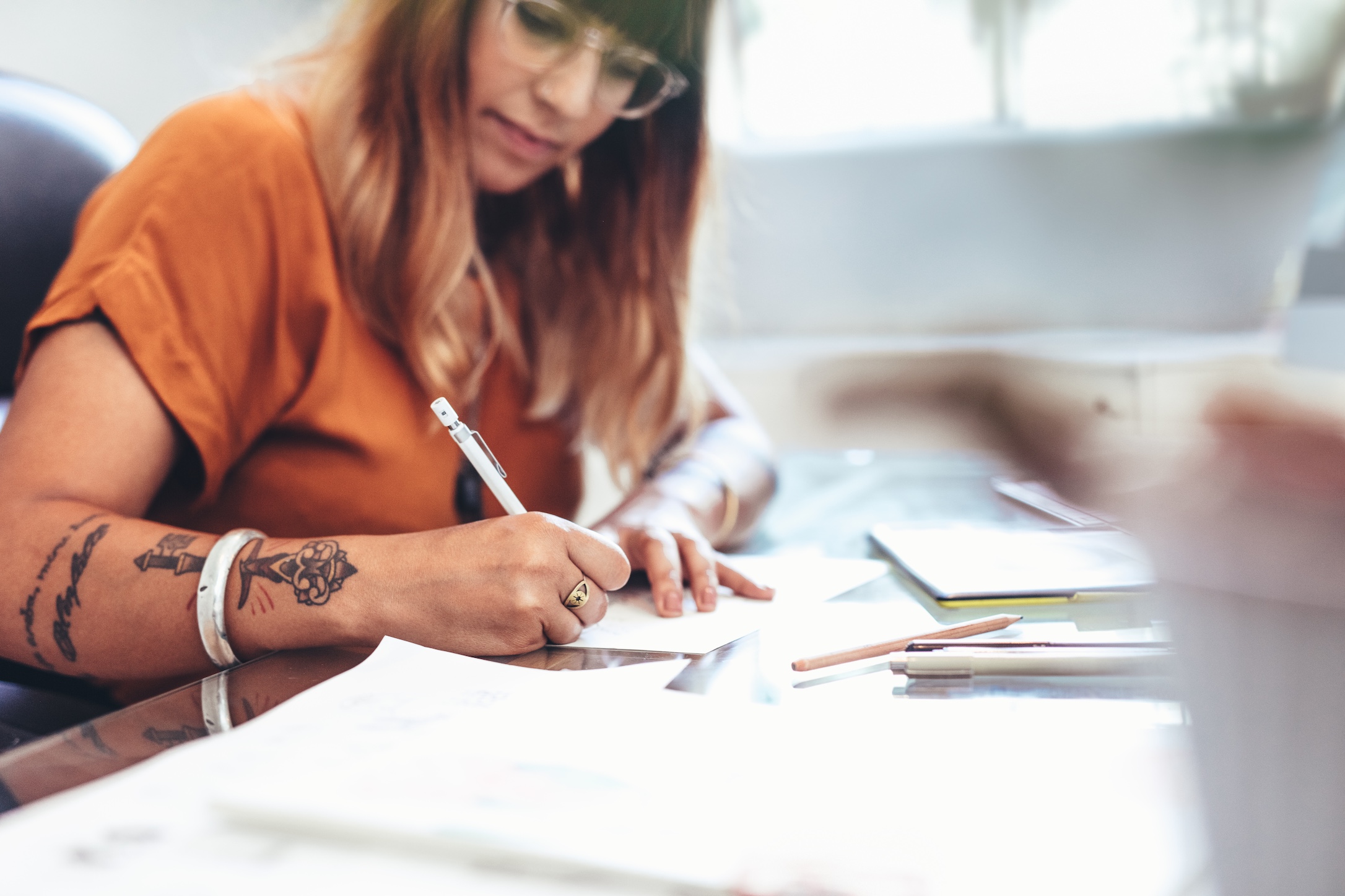 Cropped shot of a female artist making a sketch on a paper. Side view of an illustrator making a creative art sitting at her desk in office.