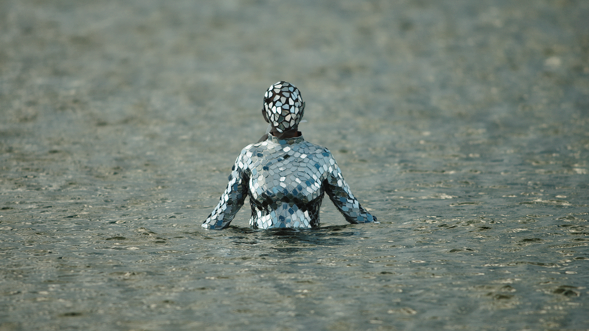 A reflective silver-tiled Carmina stands waist-deep in water, facing away
toward an expansive horizon.
Title of work: Bajo la Sombra del Sol (film still)
Artist's name: Carmina Escobar
Medium: Performance and film still