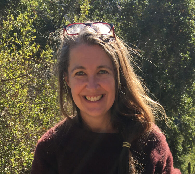 A smiling woman with long hair and a maroon sweater in the wilderness.