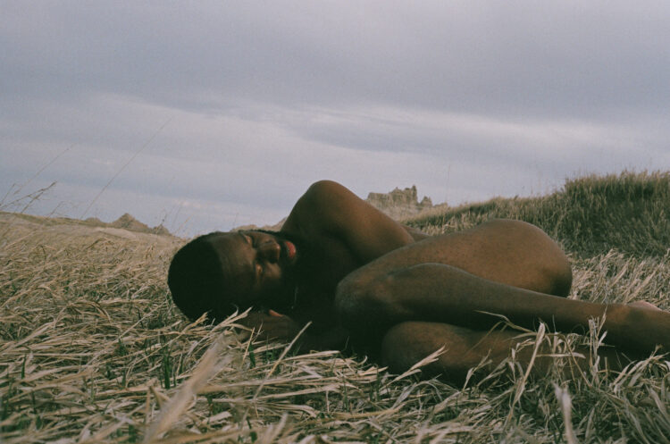 JJJJJerome lies naked and fetally curled in a field of grasses.
