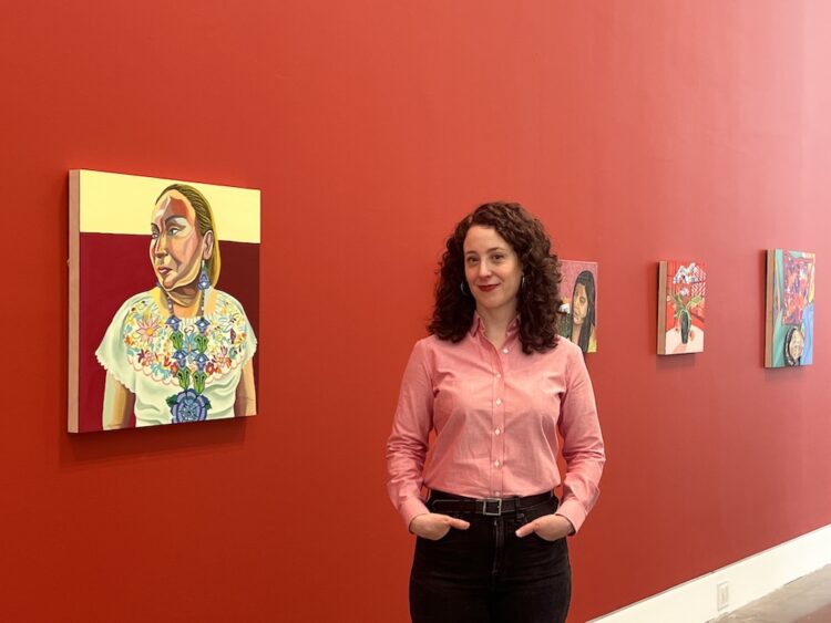 Aliza Nisenbaum headshot pic with installation of her paintings in the background.