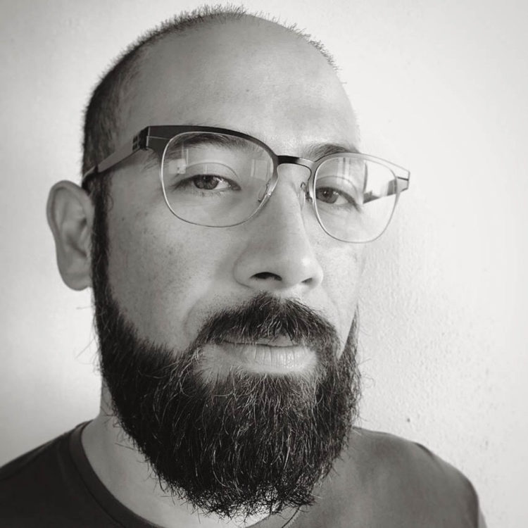 A black and white photo of a bald man with glasses and a full beard, smiling.