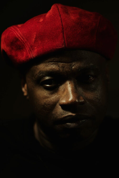 An African American man with a red suede cap turned backwards with the backdrop dimmed.