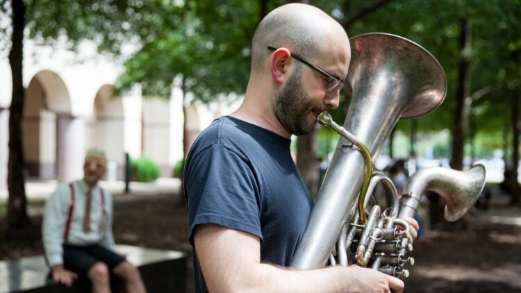 A bald, bearded white man plays a double belled euphonium with his eyes closed.