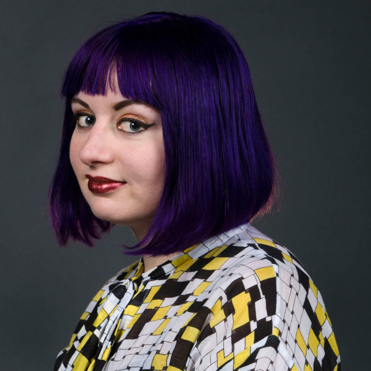 A purple-haired artist looks over her shoulder. 