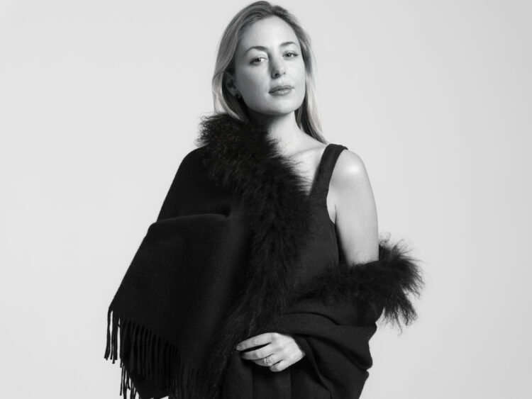 A black and white photograph of Paola Prestini, a blond woman, standing in an elegant black dress and shawl