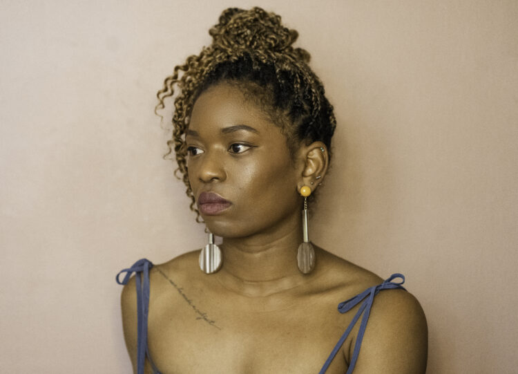 	
A portrait photograph of a black woman with brown braids in an updo in profile