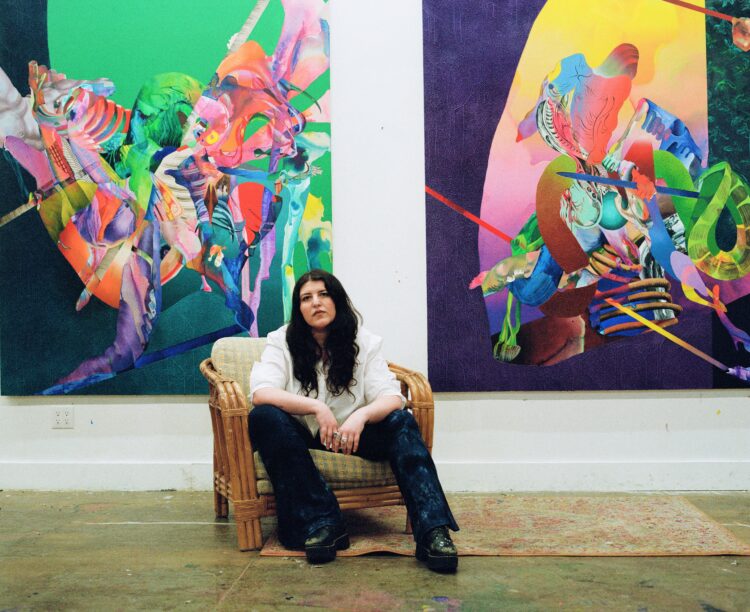 Ilana Savdie sitting in front of two paintings (Paper Planes and Spinal Sheds) in her studio.