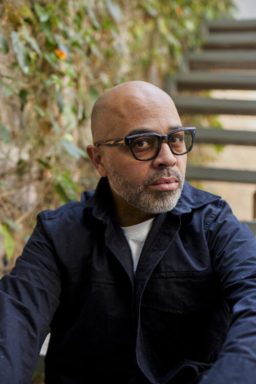 a light skinned man with glasses stares into the camera,  he is bald with a goatee.