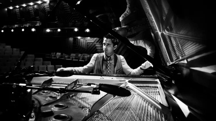 Vijay Iyer sitting at a piano with arms raised.