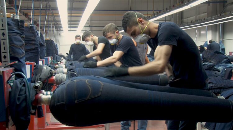 A row of men distressing jeans in an assembly line.