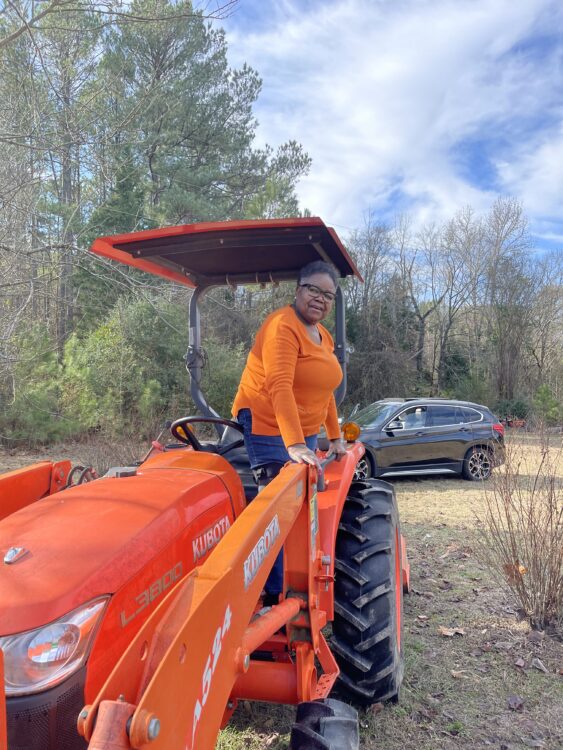 A woman in orange stands and leans over an orange tractor. 