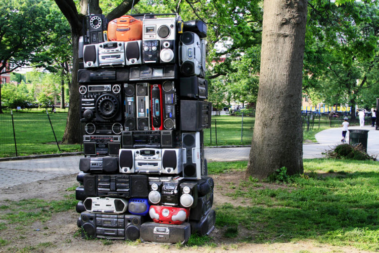 A large stack of boomboxes in a park.
